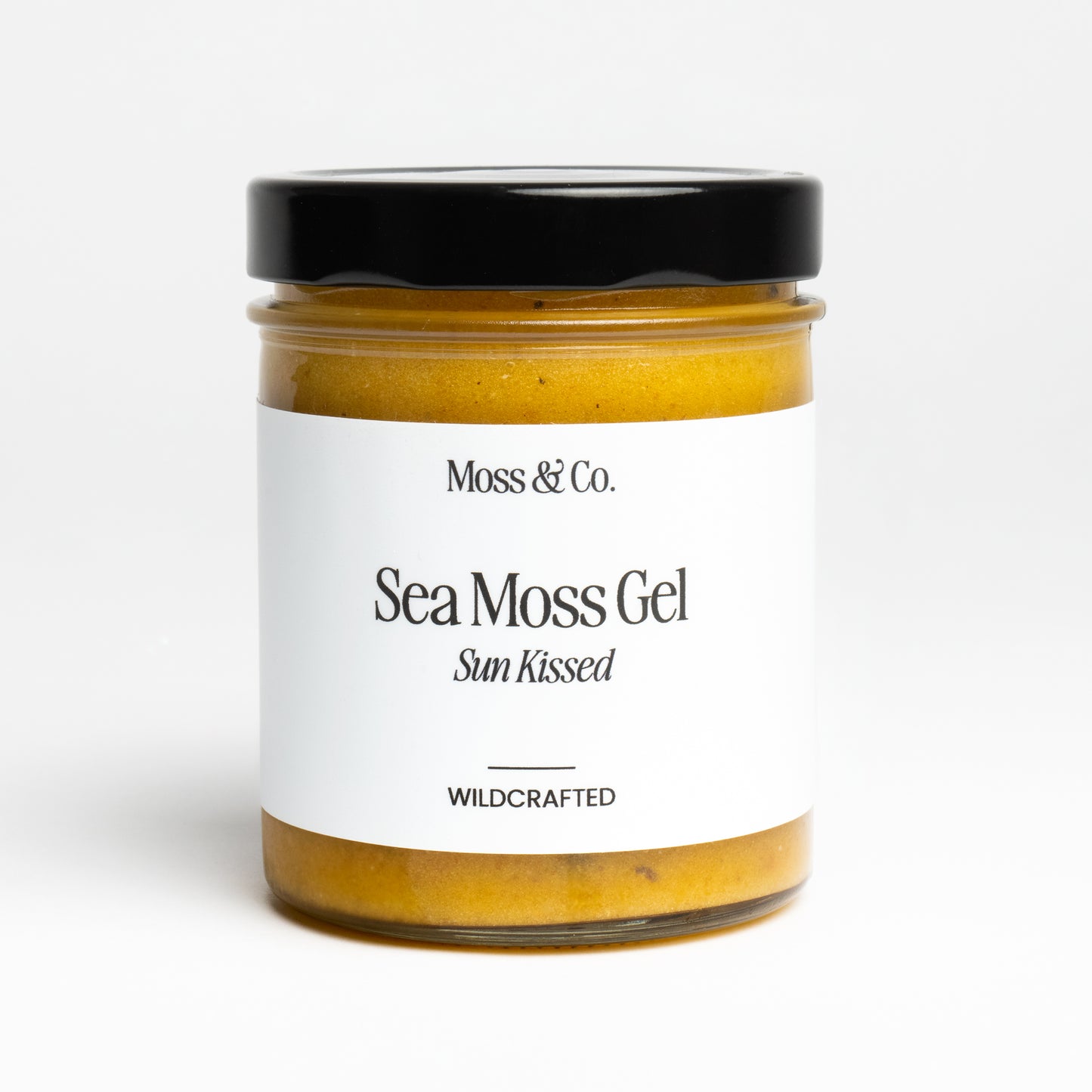 Röd flaska med Moss & Co. Sea Moss Gel i solkysst förpackning, synlig på bild.